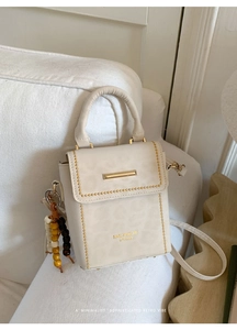 Close-up of cream square crossbody bag with gold metal trim and colorful bead charm