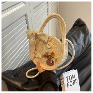 Detail of a woven round straw bag with floral embroidery and a large lace bow accent