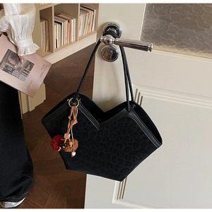 Close-up of black leopard print suede tote bag with stylish red and brown tassel charms
