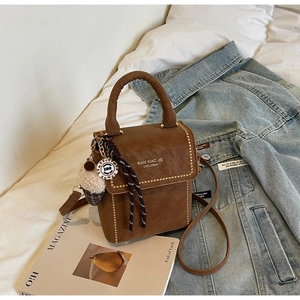 Close-up of brown textured leather bag with gold rivets, fluffy charm, and ribbon detail