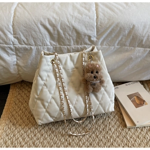 Detail of cream quilted tote bag with chain strap and cute plush bear charm decoration