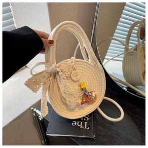 Detail of round straw bag featuring a large lace bow and floral charm for summer