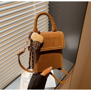 Detail of brown suede handbag featuring gold studs and a plush ice cream charm decoration