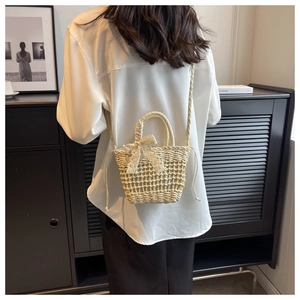 Crossbody view of a cream hand-woven straw bag with lace bow and drawstring liner