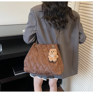 Detailed close-up of brown quilted tote bag featuring a cute bear pendant and chain strap