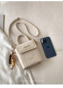 Close-up of cream square bag with gold metal trim and retro beaded charm on white fabric