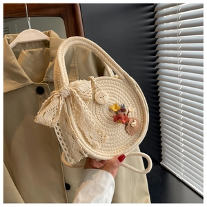 Detail of round beige woven straw bag with lace bow and colorful floral decorations
