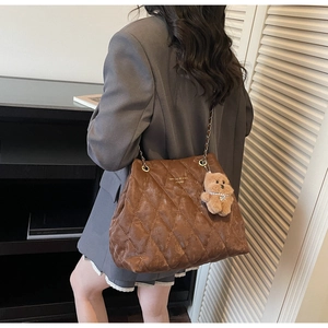Detail of a brown quilted tote bag with golden chain strap and a cute bear charm