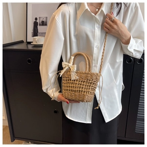 Detail of hand-woven straw bucket bag with white lace bow and woven shoulder strap