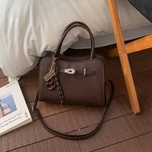 Detail of dark brown lychee leather handbag with silver twist lock and woven charm
