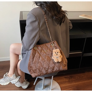 Detail of a brown quilted velvet tote bag with golden lettering and cute bear charm