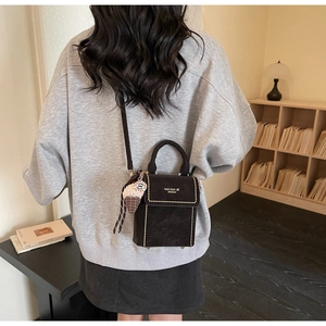 Modern dark brown crossbody bag with gold studs and knitted charm in a cozy library setting