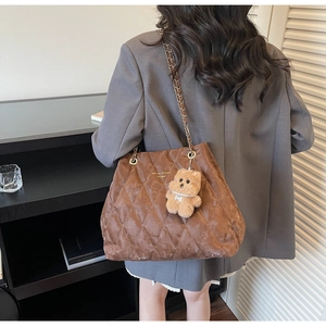 Detailed view of brown quilted tote bag with gold chain strap and cute bear charm pendant