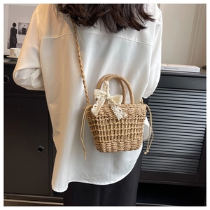 Detailed view of woven straw bucket bag with delicate white lace bow and drawstring liner