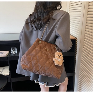 Detailed view of brown quilted tote bag featuring a cute teddy bear charm and gold logo