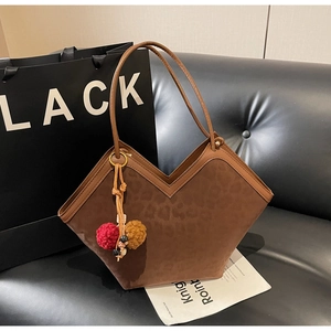 Detail of leopard embossed brown suede tote bag with colorful pompom charm on a leather sofa