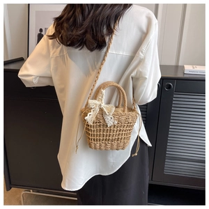 Rear view of a model wearing the beige straw bucket bag with a white lace bow detail