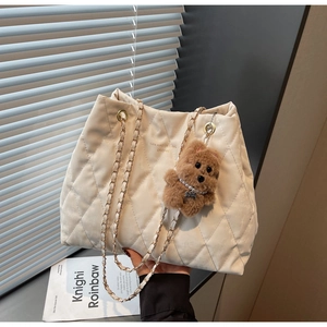 Detail of quilted tote bag with chain strap and a cute brown teddy bear keychain charm