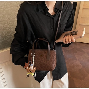 Detail of brown leopard print tote bag with bear charm and ribbon on model