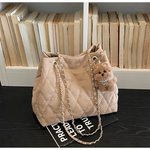 Detail of beige quilted tote bag with chain strap and teddy bear charm on wood table