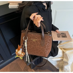Detail of leopard embossed brown tote bag with bear charm and golden logo lettering