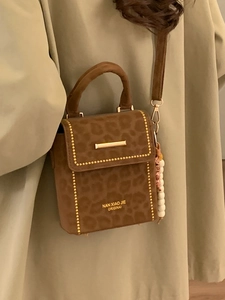 Chic leopard print crossbody bag with gold studs and beaded charm on a trench coat