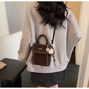 Detail of dark brown matte crossbody bag with gold studs and cream pompom charm