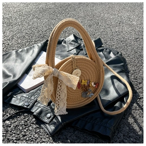 Detail of round straw bag with white lace bow and floral charms on dark asphalt