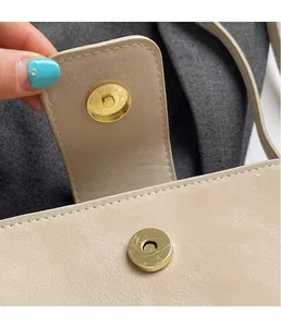 Détail de la boucle magnétique dorée et coutures fines sur un sac en cuir PU beige
