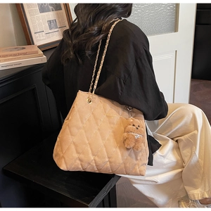 Detail of quilted apricot tote bag featuring gold lettering and plush bear accessory