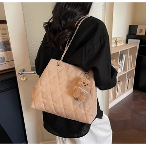 Close-up of beige quilted tote bag featuring a gold chain strap and teddy bear charm