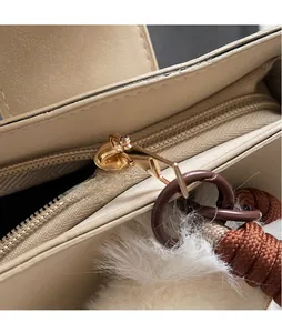 Détail du sac seau en cuir crème avec fermeture éclair dorée et pompon blanc en peluche