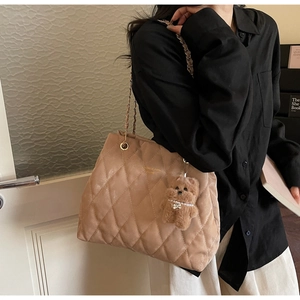 Detail of khaki quilted tote bag with gold chain strap and cute plush bear charm