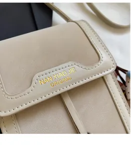 Close-up of beige leather crossbody bag featuring gold logo and lychee grain texture