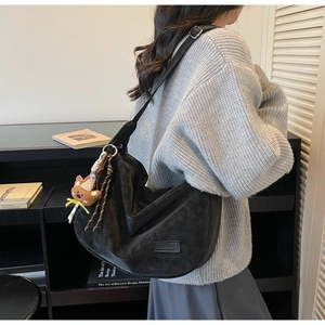 Détail du sac demi-lune en daim noir avec logo mode et pendentif ourson décoratif