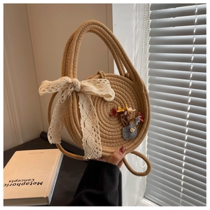 Close-up of circular straw bag with lace bow, floral applique, and dual handles