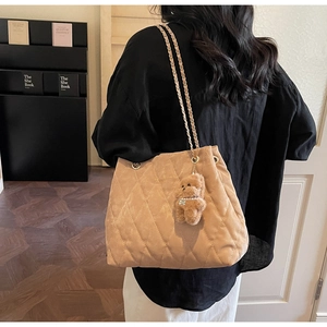 Detailed side view of khaki quilted shoulder bag with plush bear charm and metal chain strap