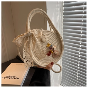 Detailed view of straw woven bag featuring white lace bow and floral charms