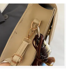 Detail of beige leather bag side with gold hardware, woven rope and plush charm