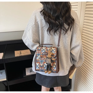 Detail of rhombic patterned crossbody bag with brown leather trim and cute rabbit charm