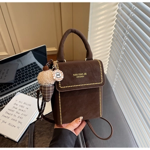 Detail of dark brown leather crossbody bag with gold studs and plush plaid charm