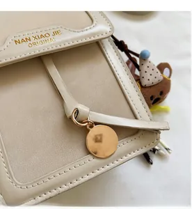 Detail of beige small square bag with golden pendant and brown teddy bear charm