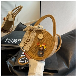 Detail of khaki straw round bag featuring lace bow embroidery and wooden button