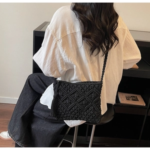 Detail of black hand-woven straw bag with geometric pattern and side tassel fringe