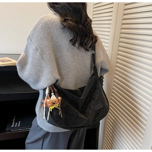 Détail du sac bandoulière croissant noir avec étiquette de mode et breloque ours en peluche