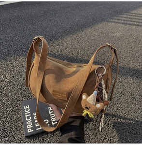 Detailed close-up of brown suede crescent bag with cute bear charm and silk scarf decoration