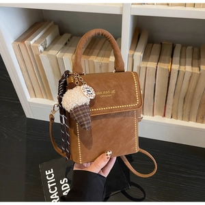 Brown leather handbag with gold studs, ice cream plush charm, and book shelf backdrop