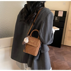 Brown vintage handbag with golden rivets and cute plush pendant on a gray suit model