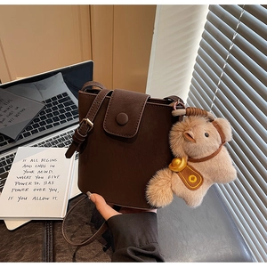 Détail du sac seau marron foncé en cuir mat avec un pendentif en peluche doux