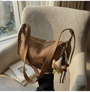 Detail of a brown slouchy dumpling bag with bear plush charm and silk scarf on a sofa